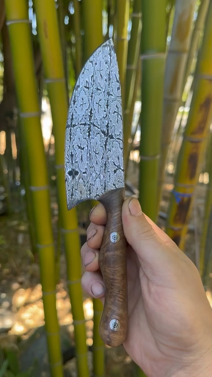 Finished pattern-welded knife with a figured wood handle held before bamboo